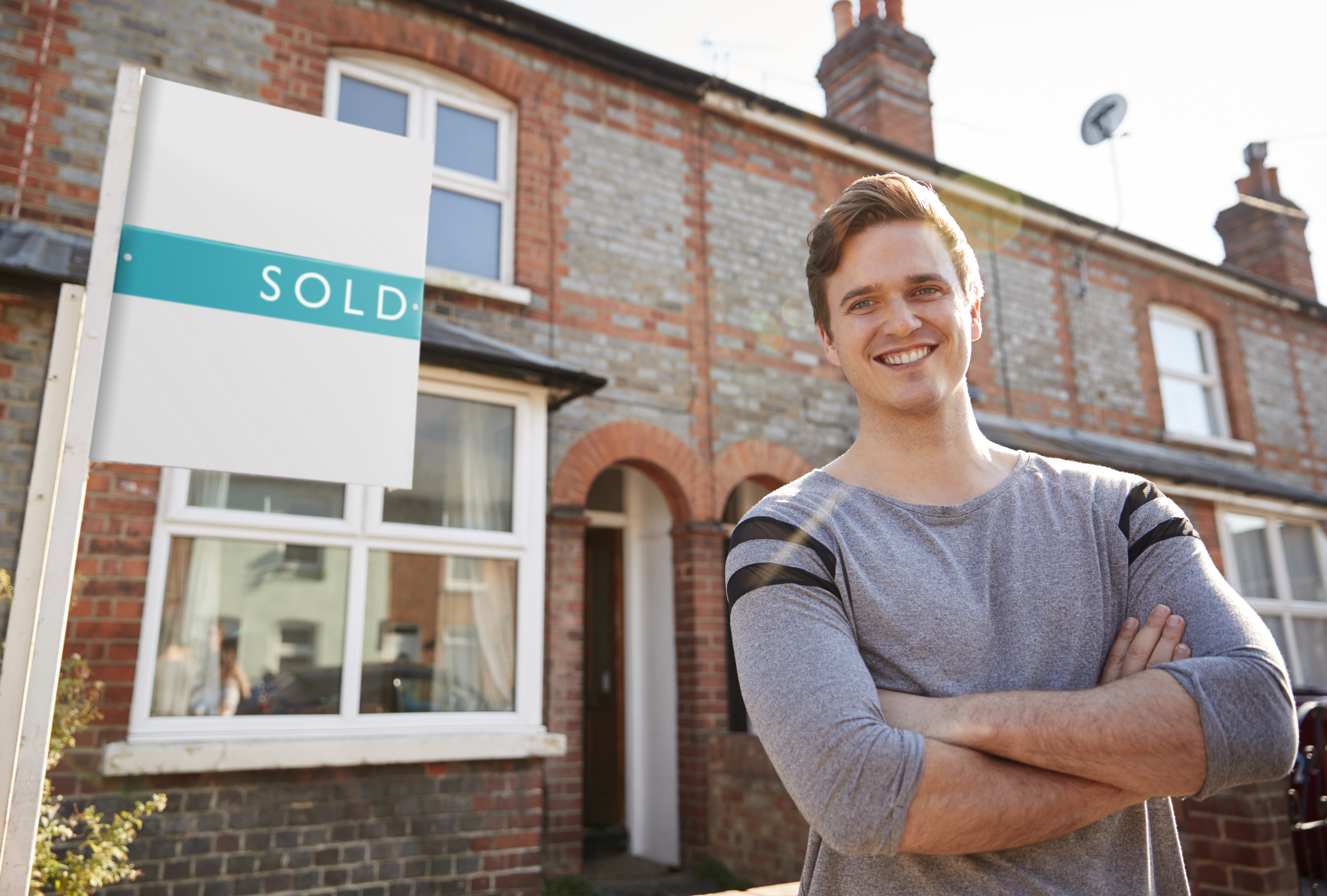 Portrait Of Excited Man Standing Outside New Home With Sold Sign